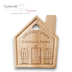 Close-up of a light-brown wooden cutting board shaped like a house, Personalised with engraved First Names and House Number.