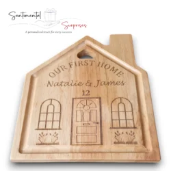 Close-up laying flat of a light-brown wooden cutting board shaped like a house, Personalised with engraved First Names and House Number.