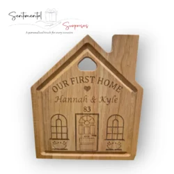 Close-up of a light-brown wooden cutting board shaped like a house, Personalised with engraved heart, First Names, and House Number.